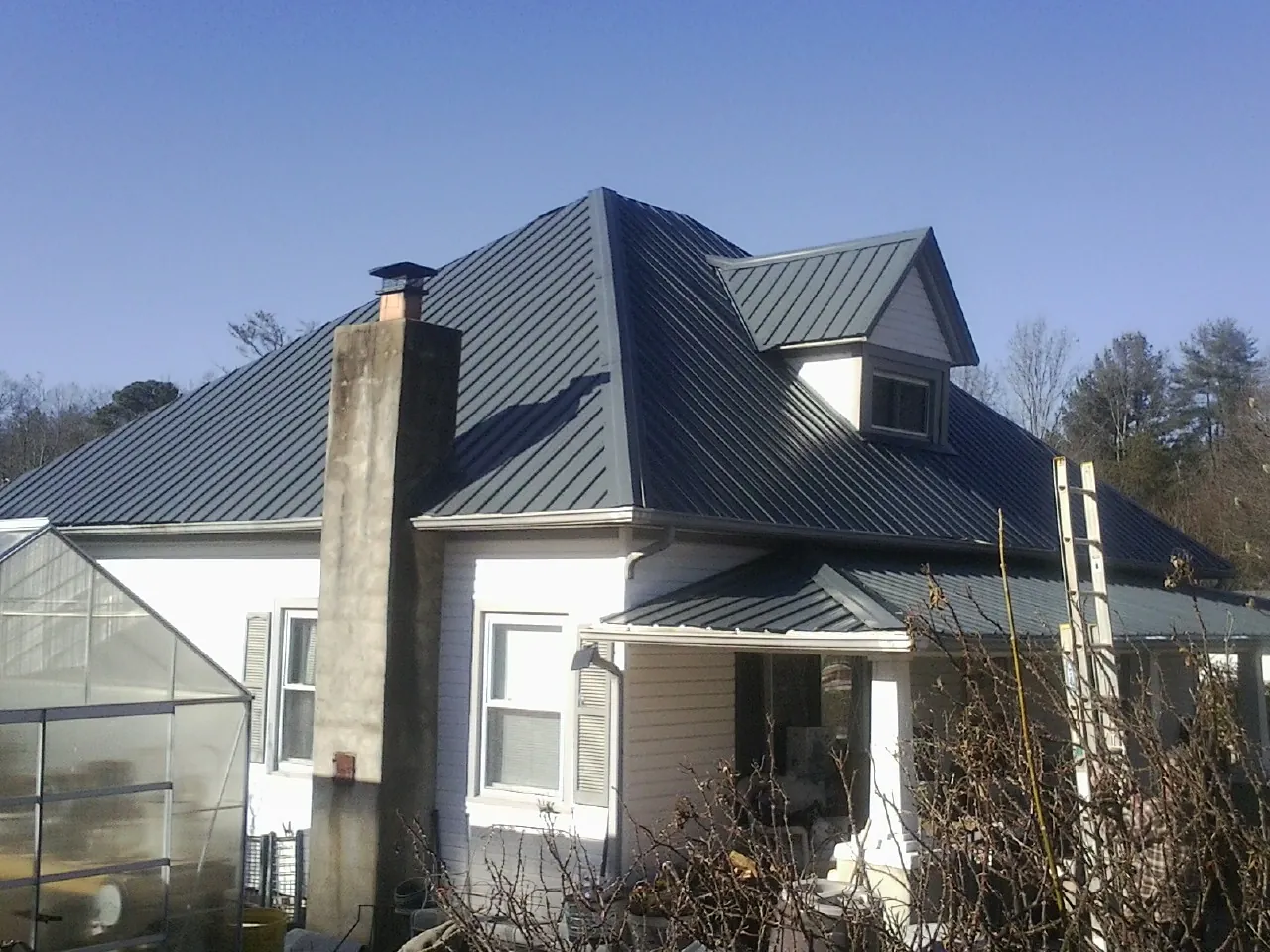 Dark blue standing seam metal roof on a white farmhouse with dormer — Slate & Tile Roof Repair by Roofing Brothers in Copiague