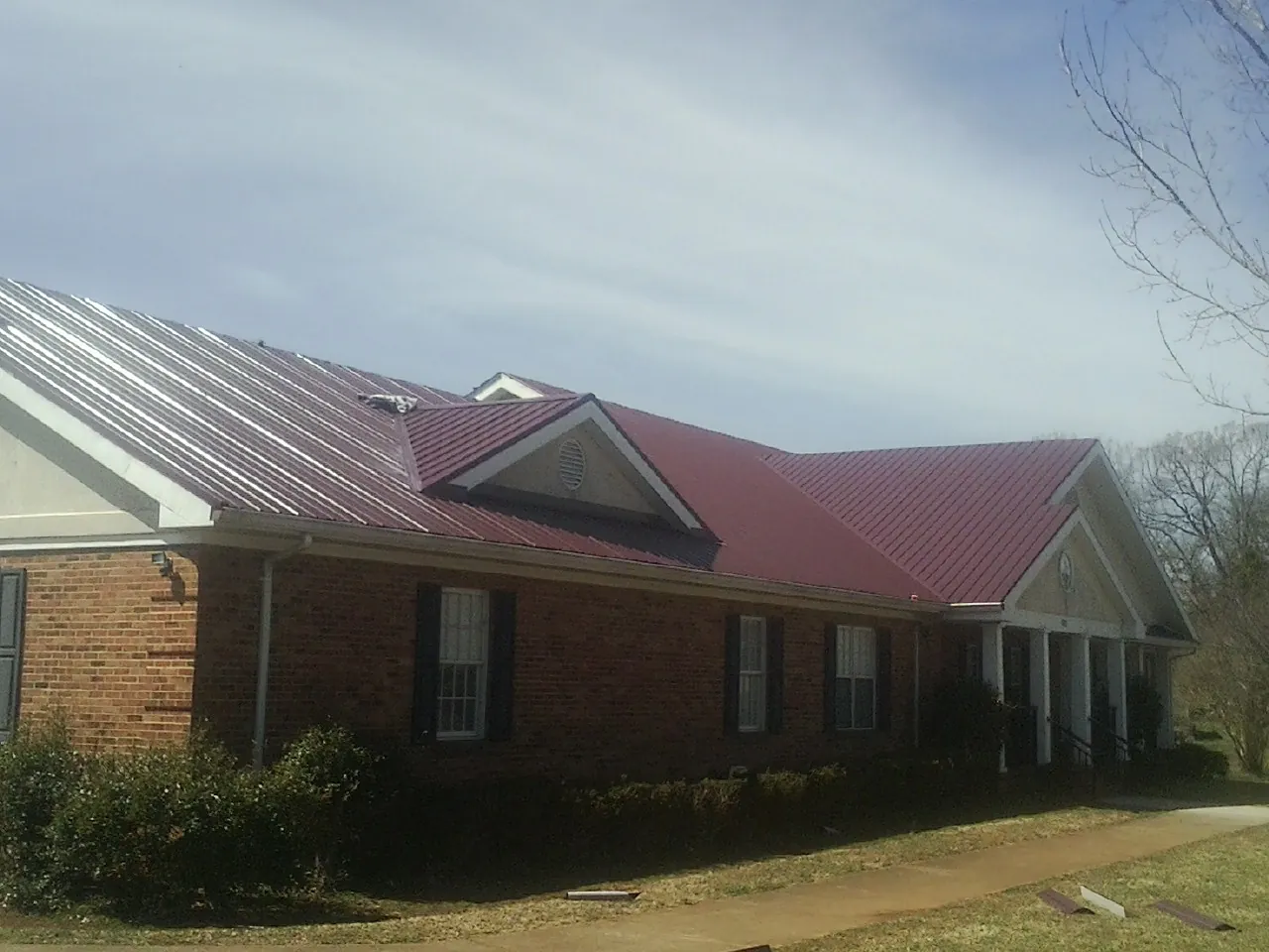Red metal roof with gabled entries on a long brick building, from a Hail Damage Roof Repair job in Copiague