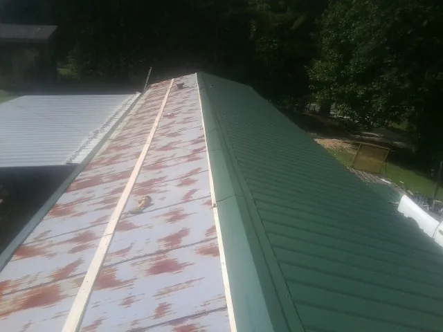 Old rusted panels beside newly installed green metal roofing — Wind Damage Roof Repair by Roofing Brothers in Copiague