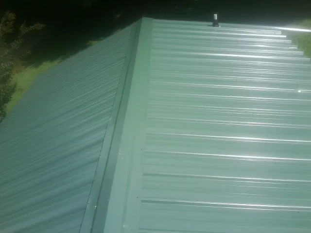 New green metal panels meeting at the ridge of a roof — Flat Roof Repair work by our crew in Copiague
