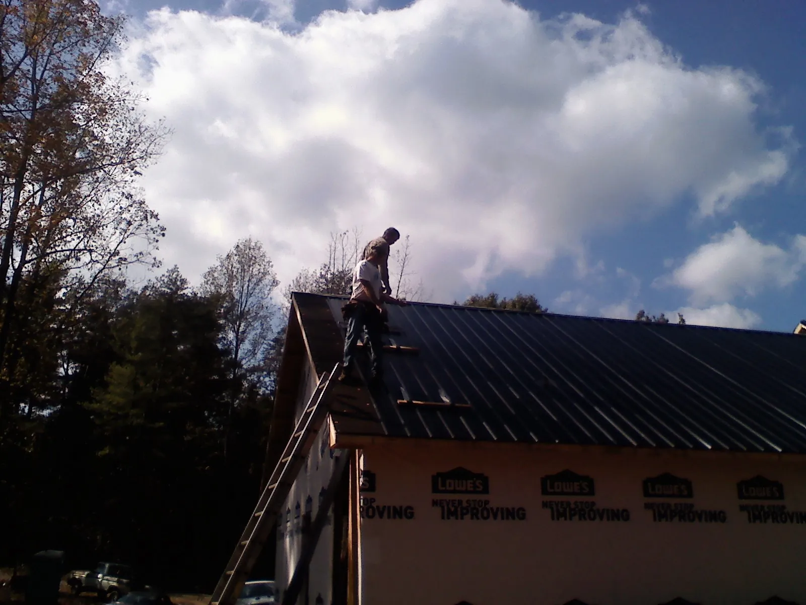 Roofer fastening dark metal panels high against a cloudy sky, from a Roof Inspection job in Copiague